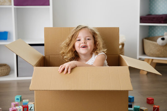 Portrait of smiling little girl sitting in cardboard box at home