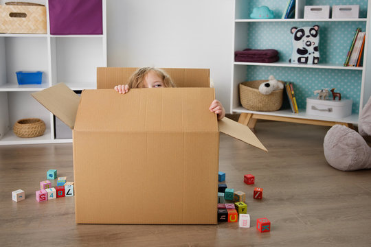 Young child peeking while sitting in cardboard box