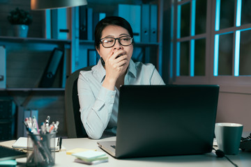 business overwork deadline and people concept. tired asian japanese woman with laptop computer working at night office and yawning. exhausted young office lady in glasses feeling sleepy cover mouth