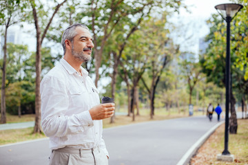 Fototapeta premium Portrait of elderly caucasian happy handsome old man drinking cup of coffee at park, Retired senior lifestyle spending time and relaxing on holidays in summer concept