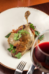 Duck leg confit with potatoes and plum and glass of red wine on wooden table at restaurant