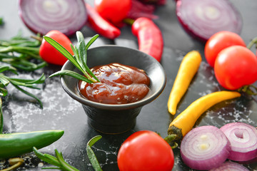 Bowl with barbecue sauce and vegetables on dark table