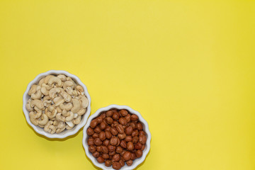 hazelnuts and cashews in two white bowls on a yellow background. the concept of proper nutrition and health. Healthy food and snack, organic vegetarian food. Walnuts, pistachios, almonds,