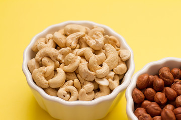 hazelnuts and cashews in two white bowls on a yellow background. the concept of proper nutrition and health. Healthy food and snack, organic vegetarian food. Walnuts, pistachios, almonds,