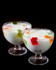 Two glasses of white milk jelly with fruit on black background. Food photography with copy space.