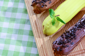 Traditional french dessert eclair pastry, three pieces laying on wooden board on a table covered with plaid fabric.