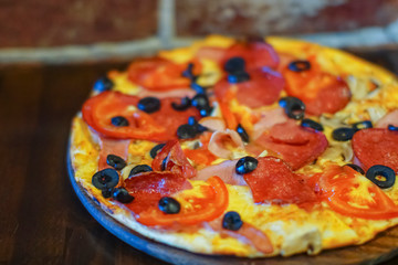 Delicious fresh pizza with meat, tomatoes, olives and mushrooms served on a board on dark wooden table, close up
