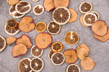 Slices of dry lemon, oranges and apples on a grey structured background