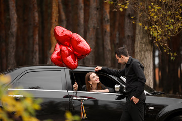 Man near his girlfriend with air balloons sitting in car. Valentine's Day celebration