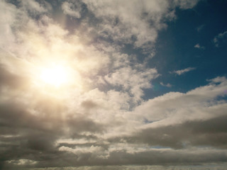 Cloudy blue sky background with sun flare and rays of light.