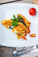 Traditional omelet with vegetables, spinach, tomatoes and herbs on a wooden table in a restaurant.