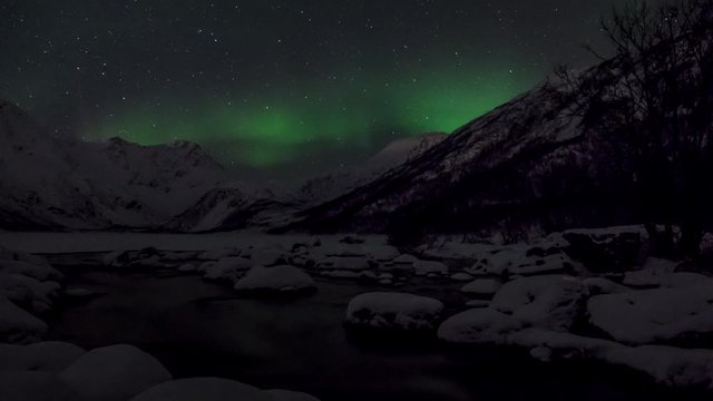 Time Lapse of Aurora Borealis, Northern Lights, and stars in Tromsoe, Norway. River in foreground and snowy mountains in background.