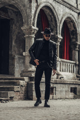 Fototapeta na wymiar Portrait of Stylish Young Man in Black Leather Jacket and Hat