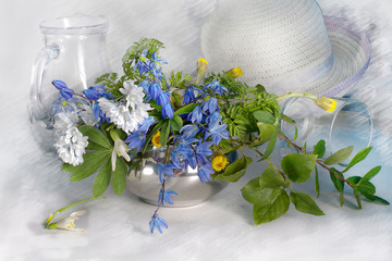 Spring flowers.A bouquet of snowdrops in a metal vase and a lady's hat on a light background