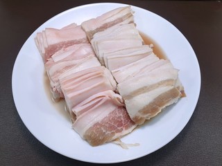 Fototapeta premium Raw meat, Top view of pork belly on white plate isolated on wooden background in restaurant, fresh meat for grill or cooking, Kurobuta Bara is japanese traditional