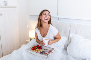 Obraz na płótnie Canvas Breakfast in bed for young beautiful woman. Woman having breakfast in bed with fruits, coffee and biscuits. Morning waking up in hotel