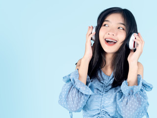 Happy Asian teenager girl using headphone on blue background.