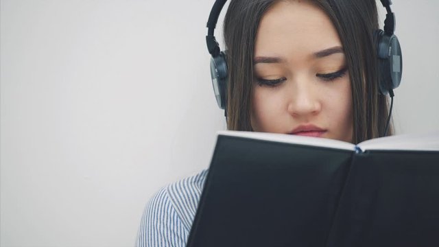 Inspired young asian girl sitting on the floor in headphones, listening to the music, writing, looking up at the camera, smiling.