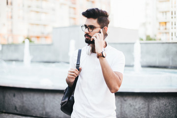 Indian handsome male student talking on the phone with bag in the street