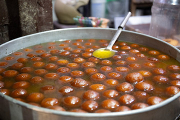 Spherical, not identified sweet deep fried balls floating in liquid. Indian street food.