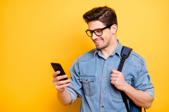 Photo of cheerful handsome attractive man browsing through telephone smiling toothily with backpack behind isolated vivid color background in jeans denim