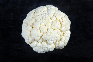 Raw cauliflower with a top side up on a black surface