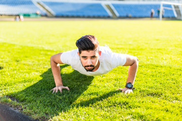 Young of indian strong shirtless man doing plank exercise at sports stadium while doing workout outdoors