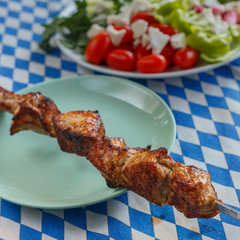 a portion of hot fried meat and a plate of fresh Greek salad on a table with a colored tablecloth