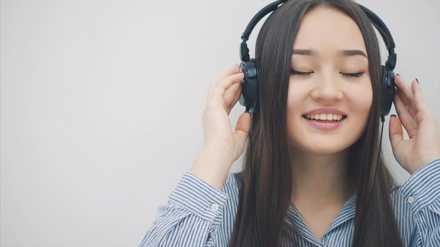 Inspired young asian girl sitting on the floor in headphones, listening to the music, writing, smiling and dancing.