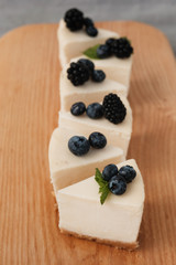 sliced cheesecake in portions with blackberries and blueberries on a wooden board. home food concept. home food concept.