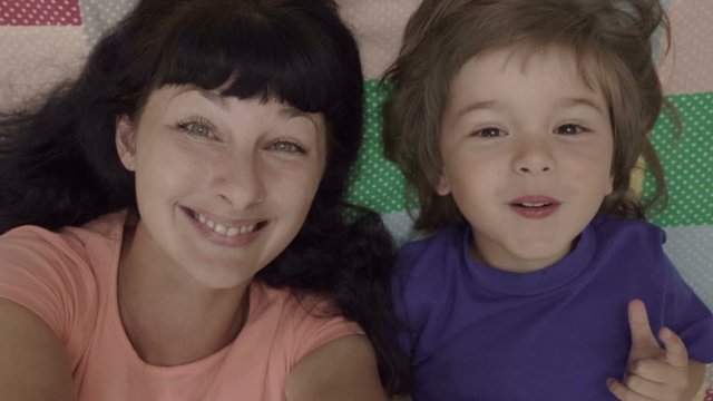 Happy Vlogger. Making Video Call. Family Selfie. Excited Young Mother and Child Playing Lying on Bed Taking Selfie. Portrait Mother and Son Monkeying on Camera Kissing. Portrait Mom and Baby. Close up