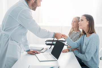 Fototapeta premium positive doctor shaking hands with mother of cute child