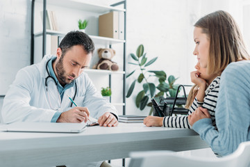 serious pediatrist writing prescription near mother and daughter