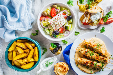 Greek food: greek salad, chicken souvlaki, gyros and baked potato wedges on gray background, top...