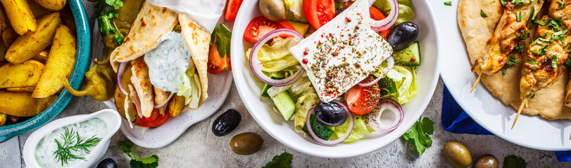 Greek food: greek salad, chicken souvlaki, gyros and baked potato wedges on gray background, top view. Traditional greek cuisine concept. - obrazy, fototapety, plakaty