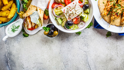 Greek food: greek salad, chicken souvlaki, gyros and baked potato wedges on gray background, top view. Traditional greek cuisine concept.