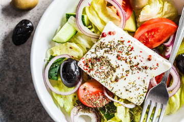 Traditional greek salad with feta, olives, tomato and cucumber in a white dish, top view.