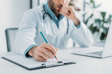 partial view of doctor writing prescription on clipboard