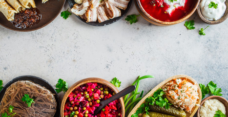 Traditional Russian cuisine concept. Borsch, jellied meat, lard, crepes, salad vinaigrette and sauerkraut, top view, banner, gray background.