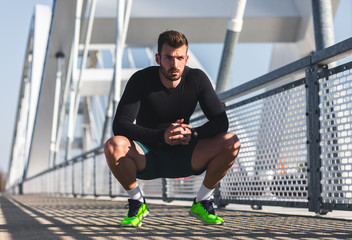 Male runner resting after morning workout on bridge.