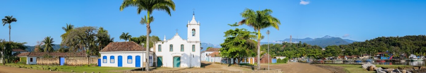 Arial view panorama of church Nossa Senhora das Dores (Our Lady of Sorrows) with palm trees and green mountains in background on a sunny day, historic town Paraty, Brazil