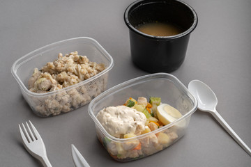 Olivier salad and oatmeal with chicken in plastic container on gray background. 45 view.