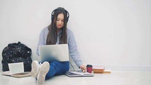 Cute asia girl sitting on the floor, involved in the process of preparation for exam. Surrounded with learning supplies.