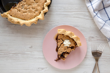 A slice of homemade Chocolate Walnut Derby Pie on a pink plate on a white wooden surface, top view. Overhead, from above, flat lay.