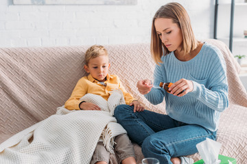 attentive mother pouring cough syrup in spoon while sitting near sick son