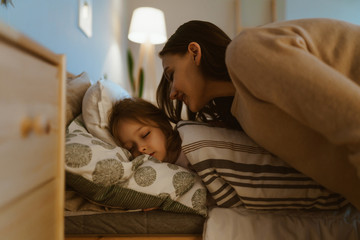 the girl sleeps in bed, mom came to wake her up and gently leaned over her - 309913127