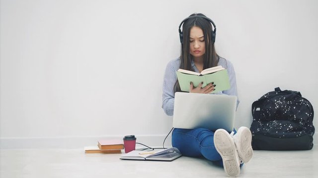 Cute asia girl sitting on the floor, involved in the process of preparation for exam. Surrounded with learning supplies.