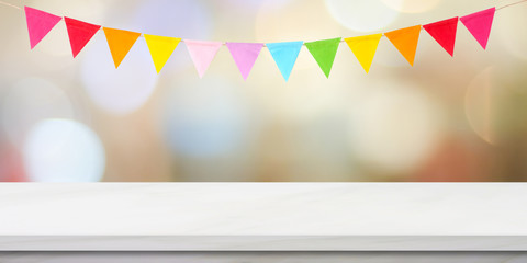 Colorful bunting party flags hanging onblur abstract bokeh light and white marble table background,...