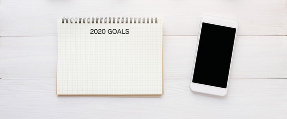 2020 goals on blank note paper and smart phone with blank screen on white marble background, 2020 new year aim to success in business background