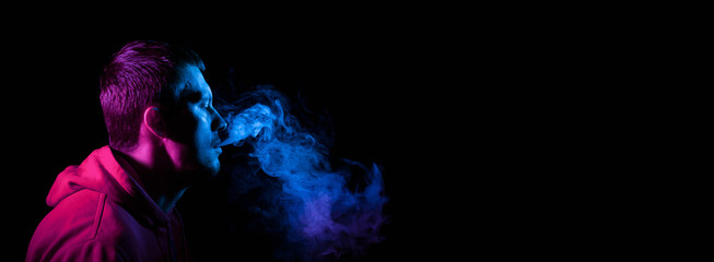 Close up portrait of the face of an adult serious man exhales blue toxic smoke while smoking...